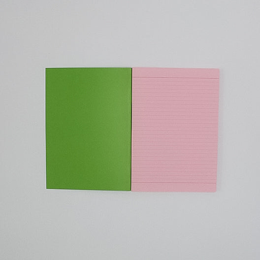An open A5 notebook, with a bright green inside the cover, and light pink tinted inner pages with dark pink printed lines. 