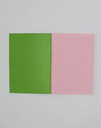An open A5 notebook, with a bright green inside the cover, and light pink tinted inner pages with dark pink printed lines. 