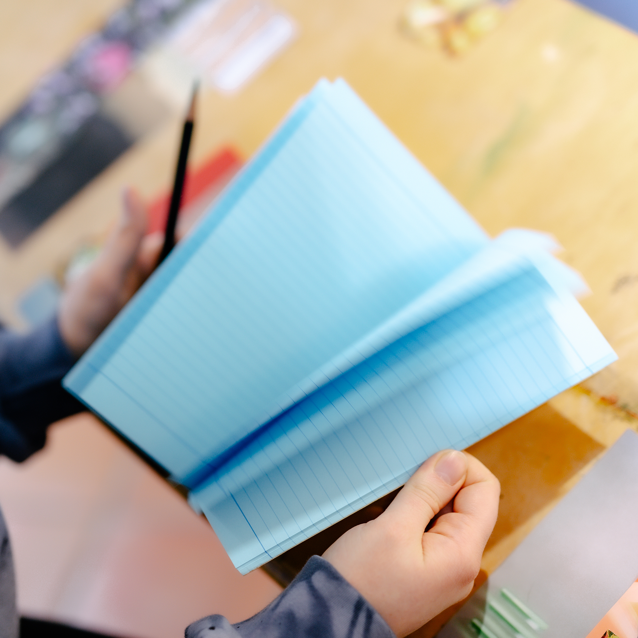 Hands flipping through a blue paper socolo A5 notebook at a wooden desk.